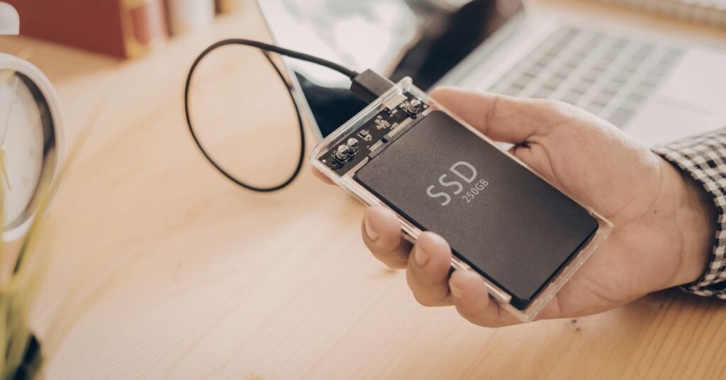 Holding ssd in hand near laptop and magnifying glass on wooden desk